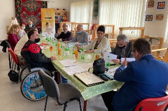 Slika.Koalicija organizacija osoba sa invaliditetom Grada Bijeljine KOLOSI, održala je sastanak 25. februara 2021. godine u prostorijama Udruženja žena sa invaliditetom „IMPULS” Bijeljina, MZ Galac. Na slici su predtavnici udruženja koja čine koalciju, koji sjede za stolom, jedan od predstavnika je korisnik kolica za osobe sa invaliditetom.
