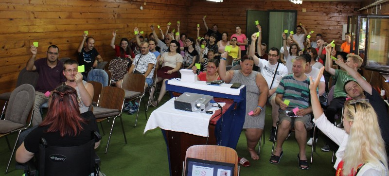 Slika nastala tokom predavanja Selme Plančić, koja je okrenuta lprema učesnicama i učesnicima koji u u podignutoj ruci drže žute papiriće.