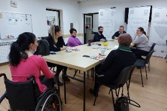 Slika. Partnerska organizacija Informativni centar za osobe s invaliditetom „Lotos“ Tuzla 11. februara 2021. godine održala je sastanak sa predstavnicama Zavoda za odgoj i obrazovanje osoba sa smetnjama u psihičkom i tjelesnom razvoju Tuzla i Vijeća roditelja. Na slici su predstavnici IC Lotos zajedno sa predstavnicama Zavoda i Vijeća roditelja koji sjede za stolom u prostorijama IC Lotos.